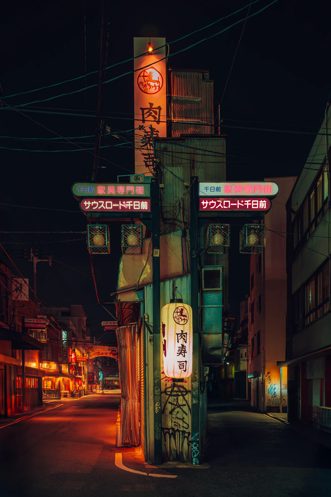 Angle de rue avec un haut poteau d’enseignes, une lanterne de papier allumée et des arches au néon en japonais, lignes électriques au-dessus, la nuit.